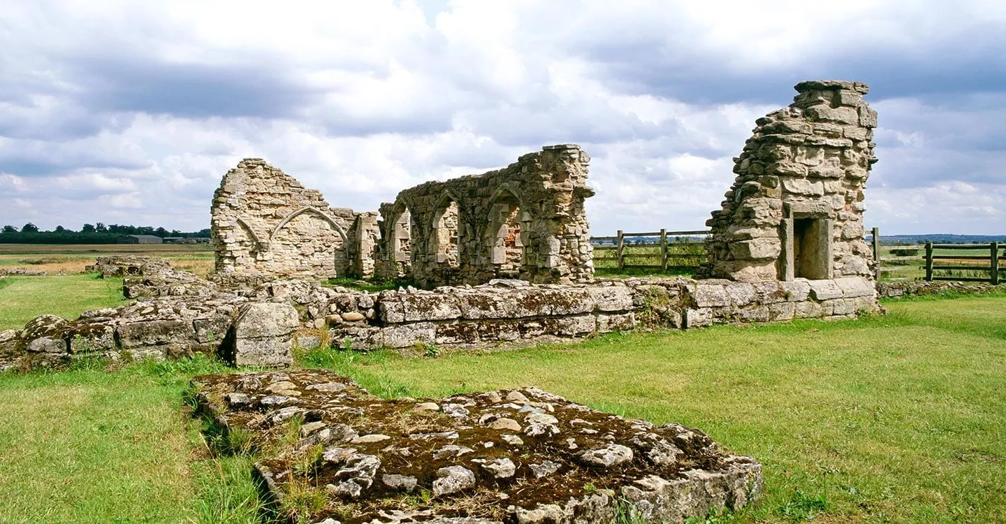 The ruined stone walls and arcade of Mattersey Priory on a green lawn, with flat farmland and a cloudy sky beyond