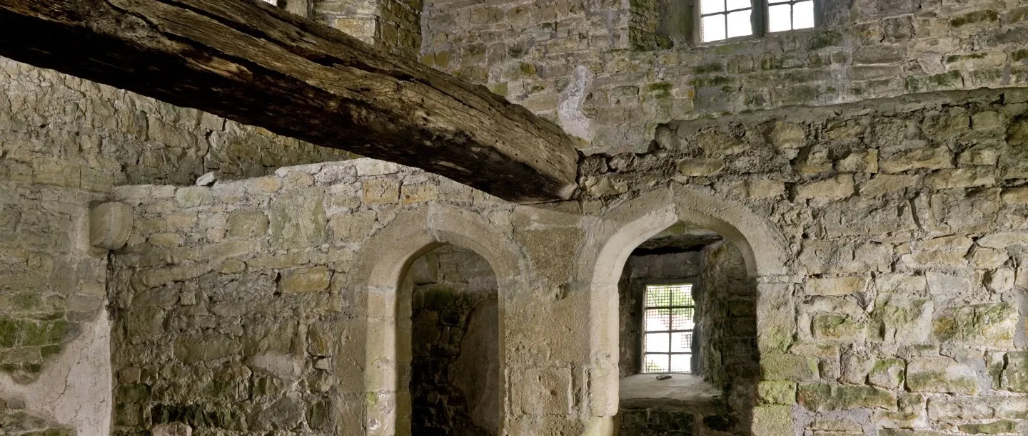 Inside Meare Fish House, a massive timber beam across bare stone walls above two arched window recesses