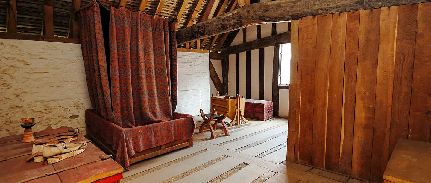 The upper chamber of the Medieval Merchant's House, with a curtained bed, folding chair, chest and open timber roof
