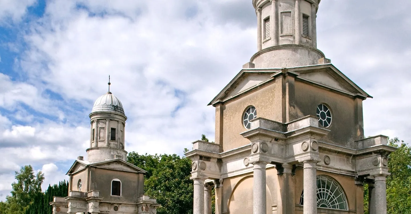 The two pale classical towers of Mistley, each with a columned portico and a domed cupola, against a blue sky with white clouds