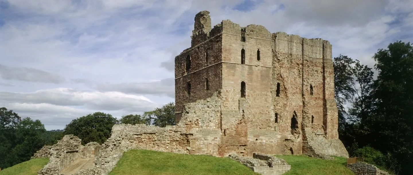 Norham Castle's tall sandstone keep beside the low ruined walls and stone stair of the inner ward, under a cloudy sky
