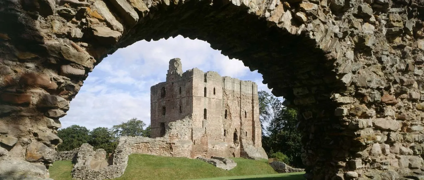 The great tower of Norham Castle framed by a ruined stone arch, with grassy inner ward and trees beyond