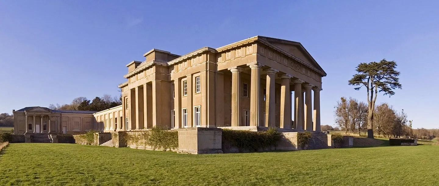 The Grange at Northington, a Greek Revival mansion with a massive Doric portico, beside a lawn and a tall cedar under a clear blue sky