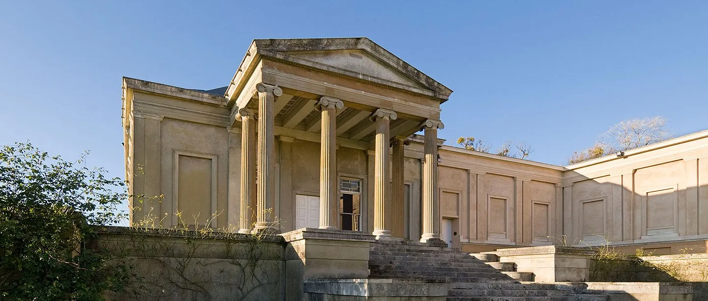 The Ionic portico and wide stone steps of the orangery wing at The Grange, Northington, in warm sunlight against a blue sky