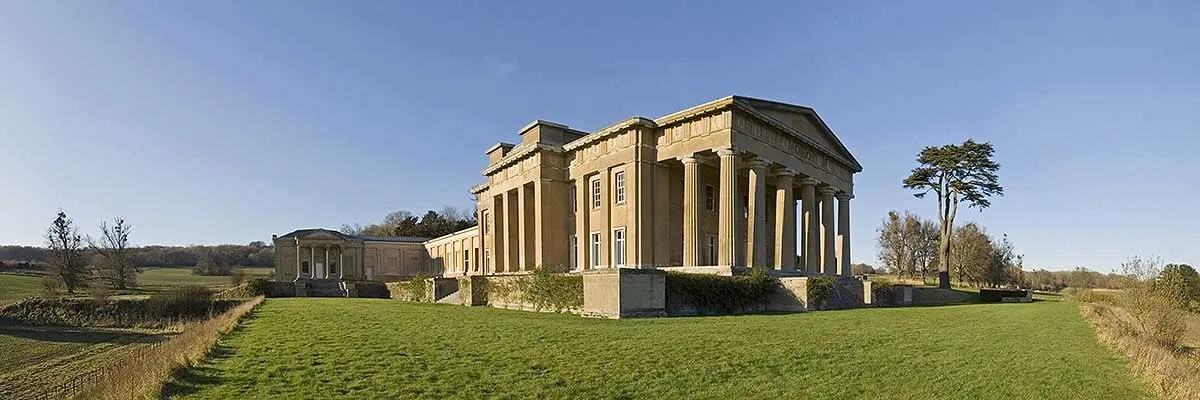 A panoramic view of The Grange at Northington and its long wings across a broad lawn, with parkland and fields on either side