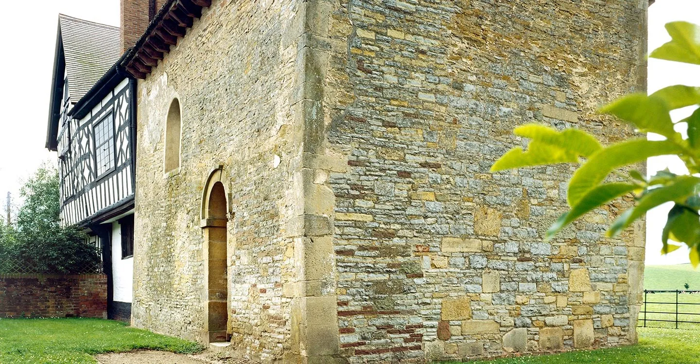 The rubble stone walls and round-headed doorway of Odda's Chapel, a Saxon chapel joined to a timber-framed farmhouse