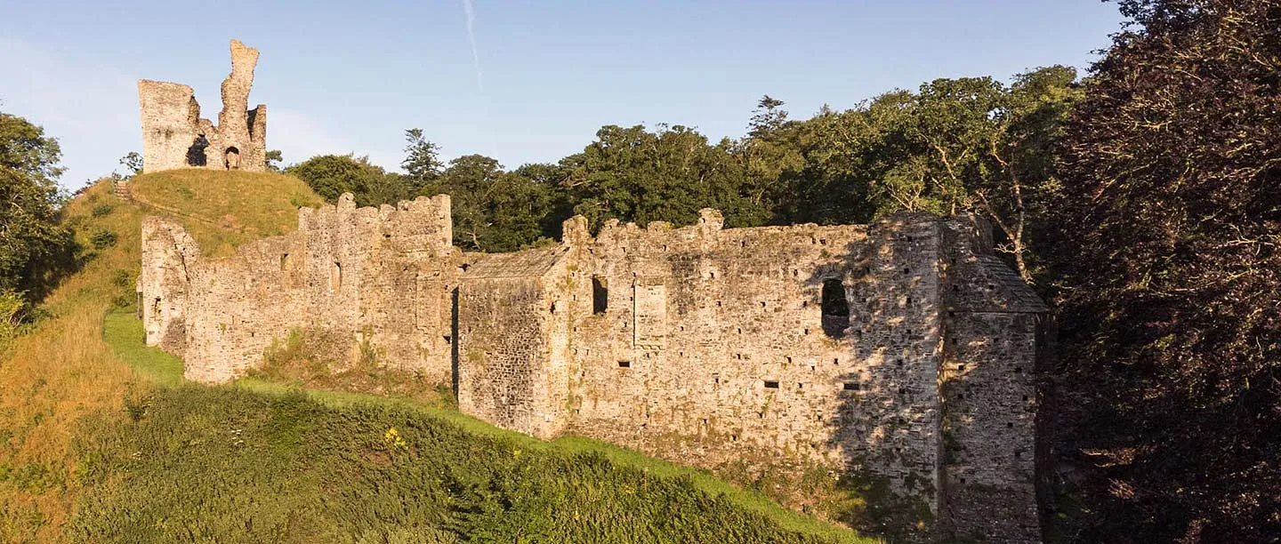 Okehampton Castle's long curtain walls and ruined keep on its motte, lit by warm evening sun
