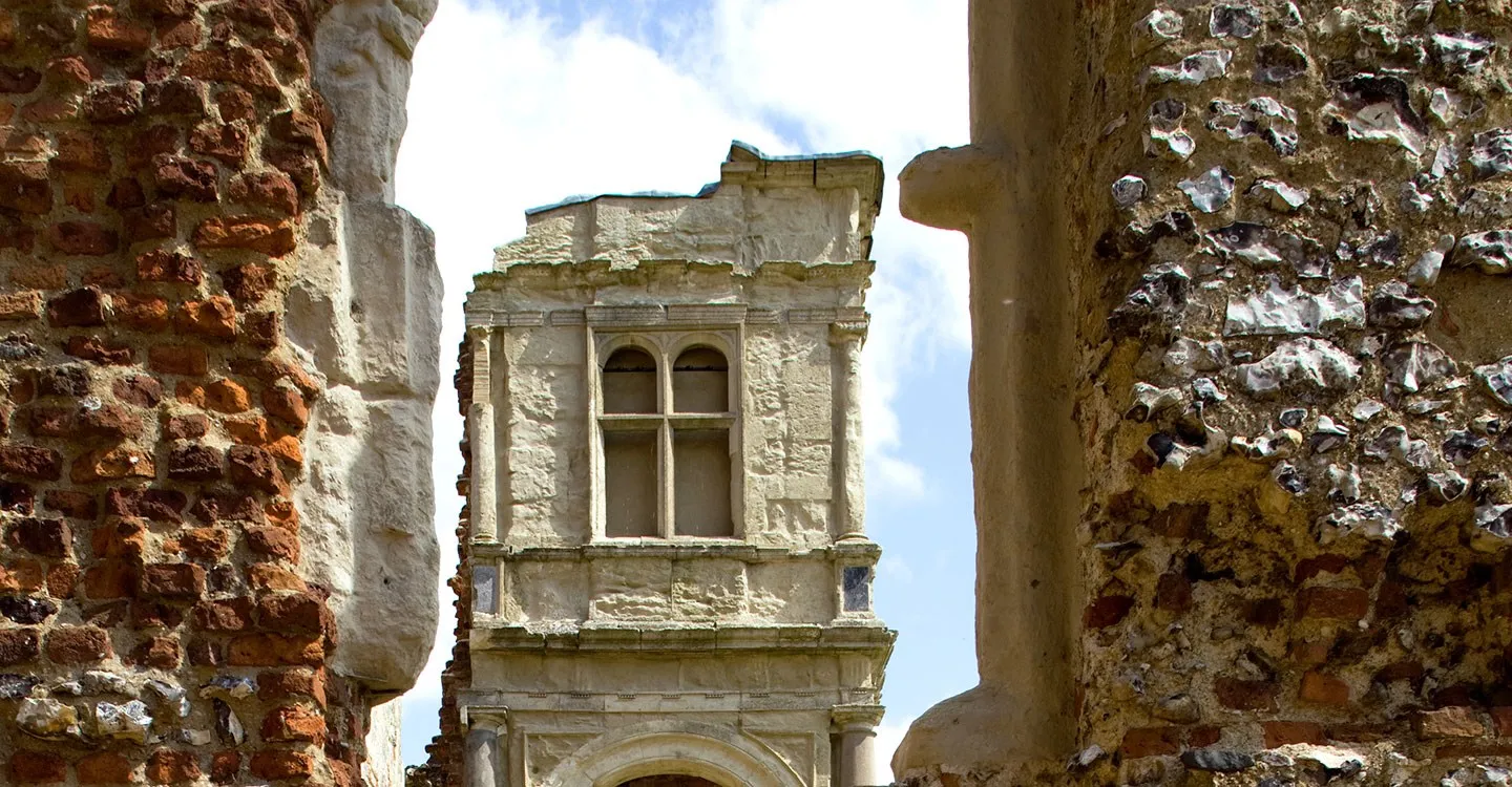 The carved upper storey of Old Gorhambury House's porch framed between ruined brick and flint walls