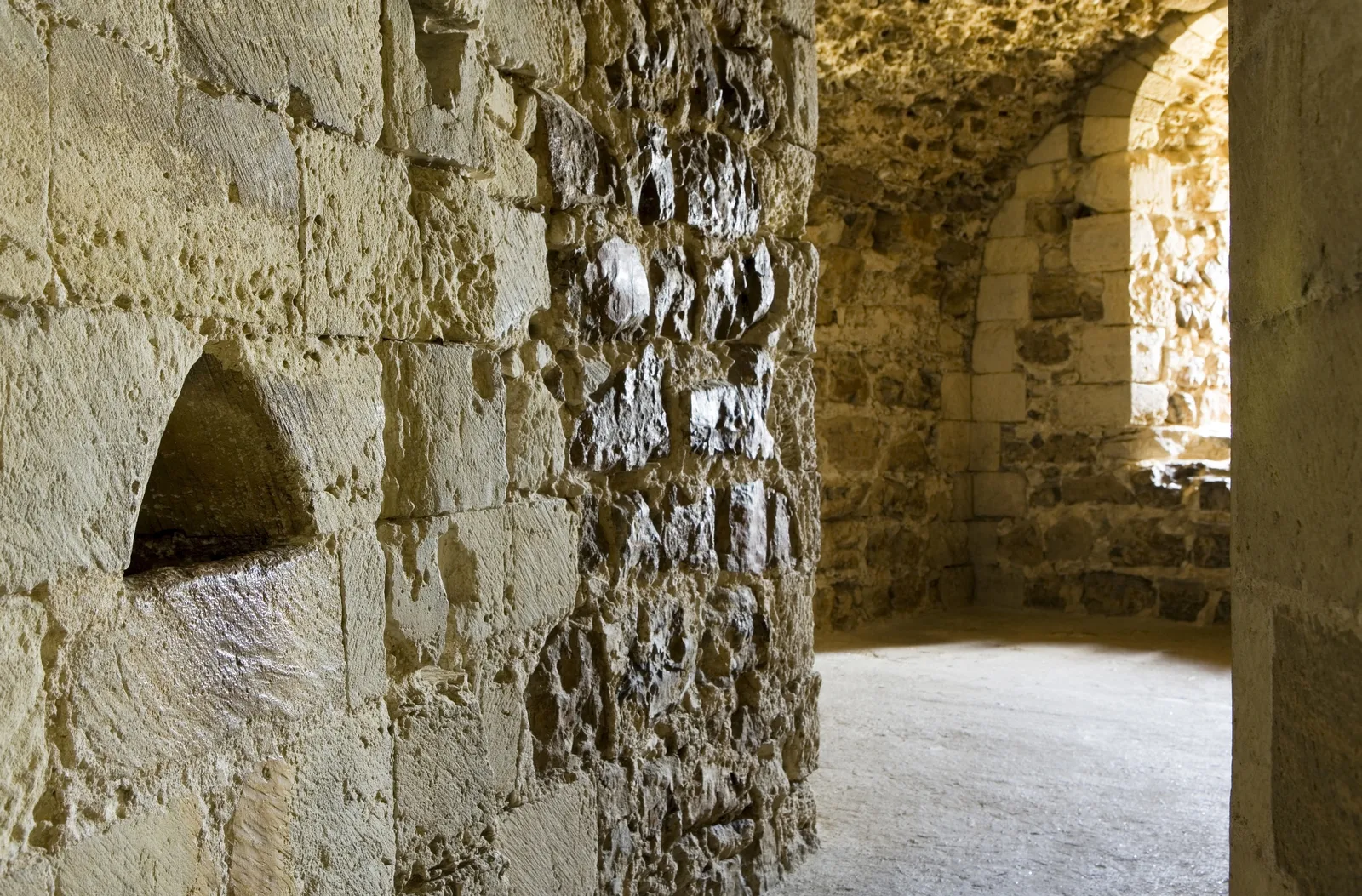 Worn stone walls and a lit chamber inside a passage in the thickness of the keep