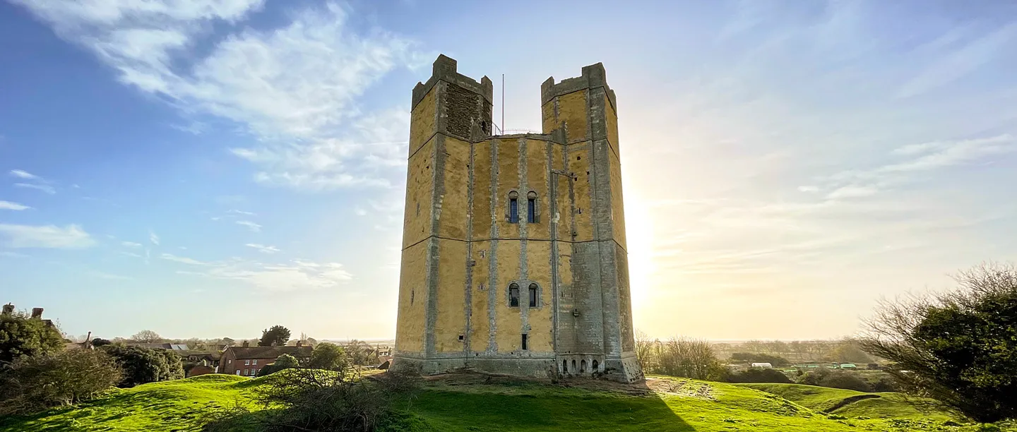 The tall polygonal keep of Orford Castle against low sun, with the village rooftops beyond