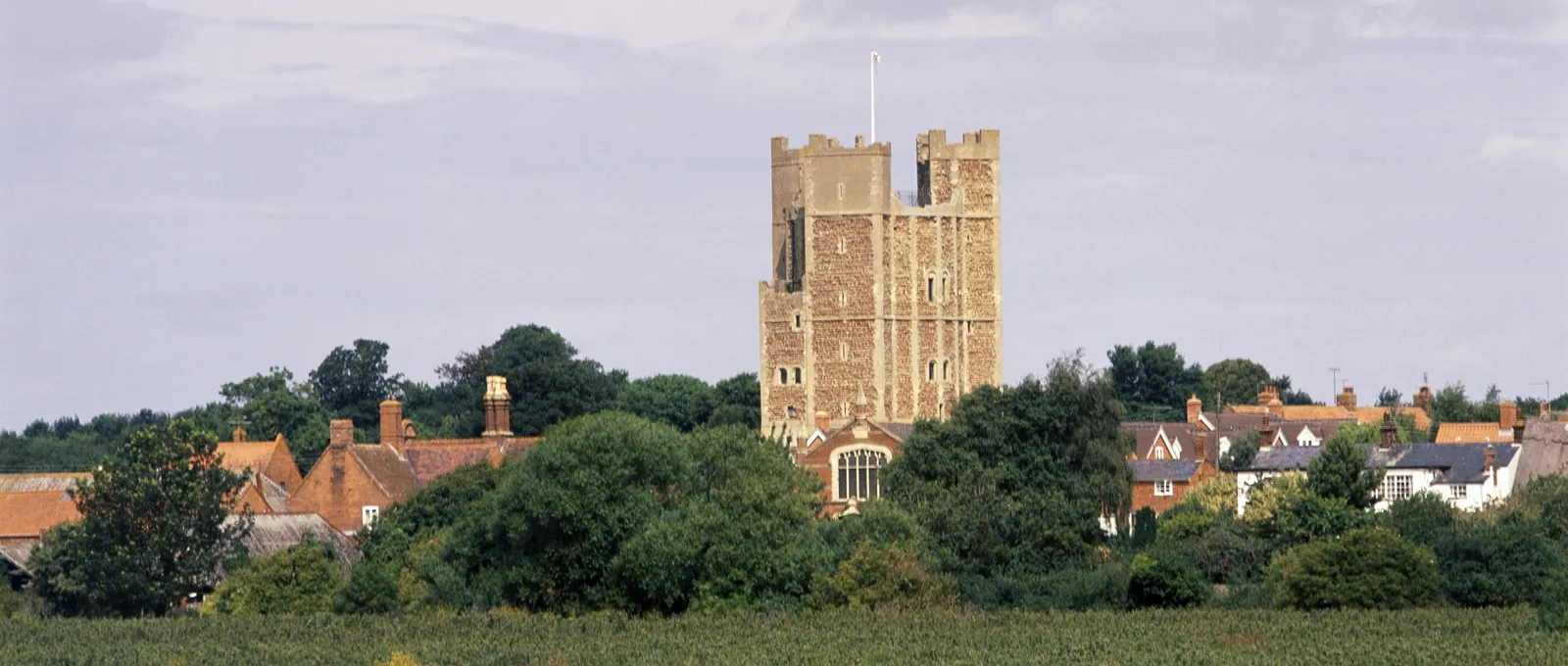 The keep rising above trees and village roofs, seen across a field