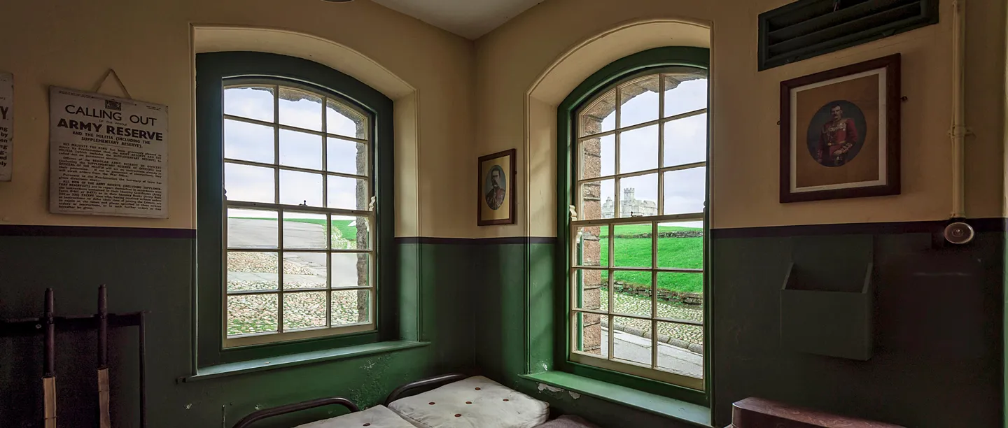 A barrack room with a sash window looking out to the castle, army notices and a portrait on the walls