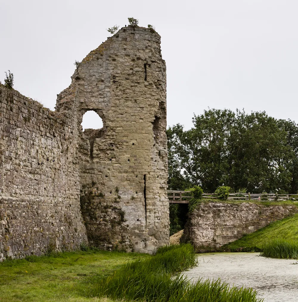 The gatehouse's broken tower beside the moat and footbridge on a grey day