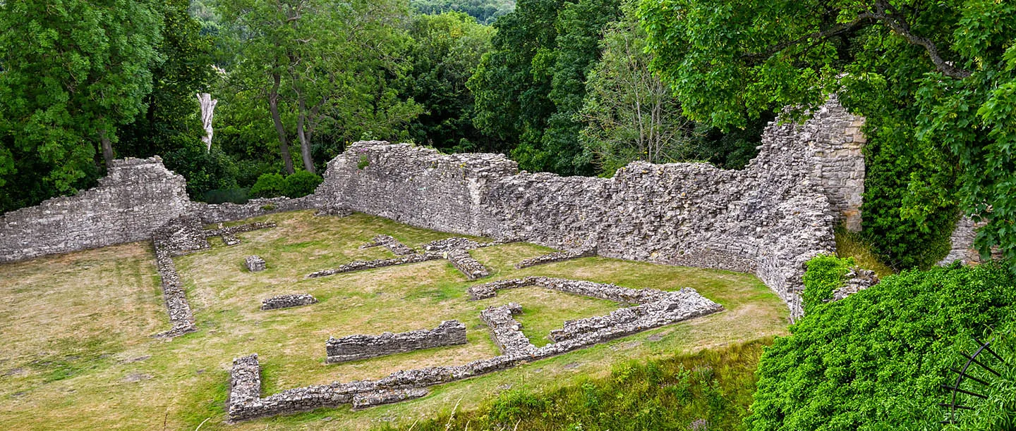 Low wall foundations of the castle's lost buildings inside the curtain wall, ringed by trees