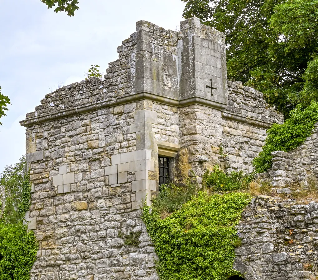 The restored stone chapel with a cross on its buttress among ivy and trees