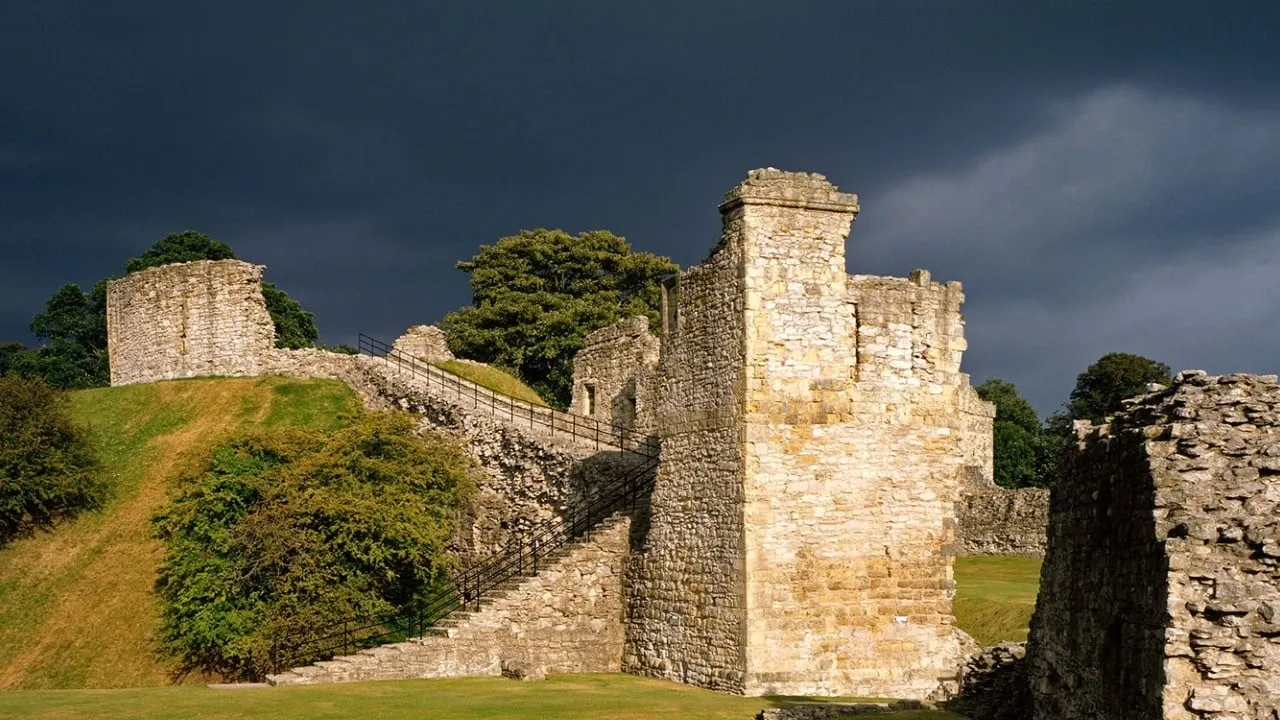 Sunlit ruined towers and the steps up the motte to the keep under a dark storm sky