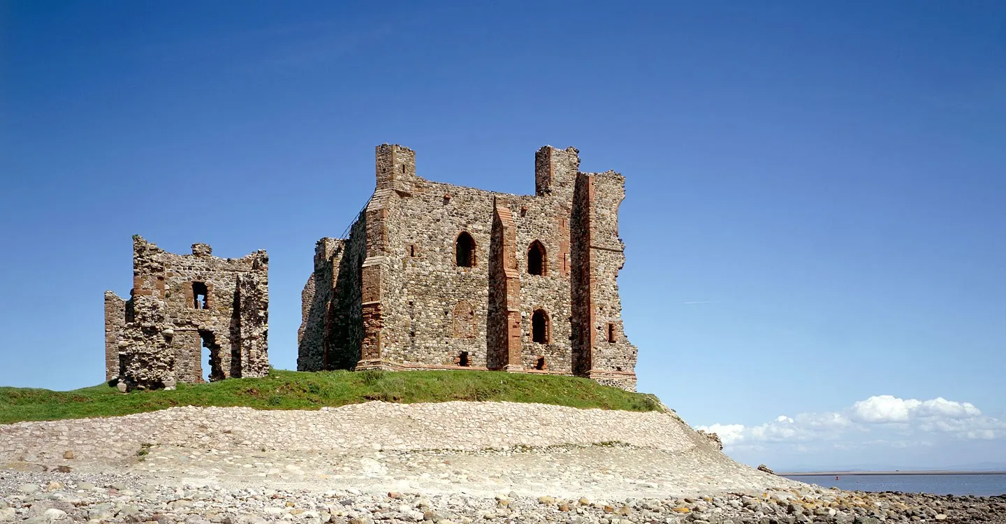 The ruined keep and gatehouse of Piel Castle above a shingle beach on Piel Island, under a deep blue sky