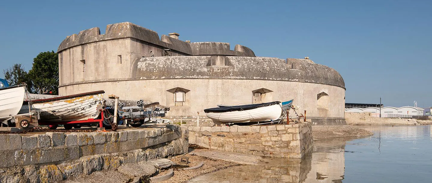 Boats drawn up on the slipway below the castle's rounded seaward walls, mirrored in still water