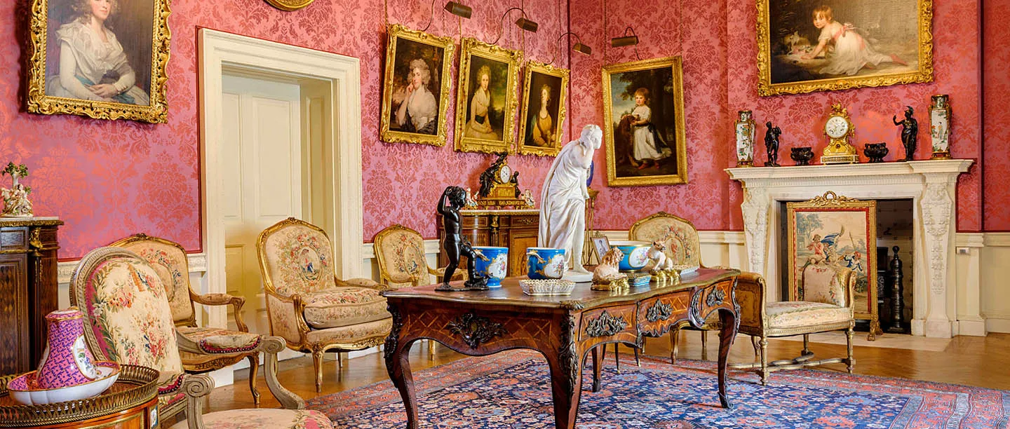 A red damask room at Ranger's House hung with gilt-framed portraits, with tapestry armchairs, a marble statue and an inlaid writing table