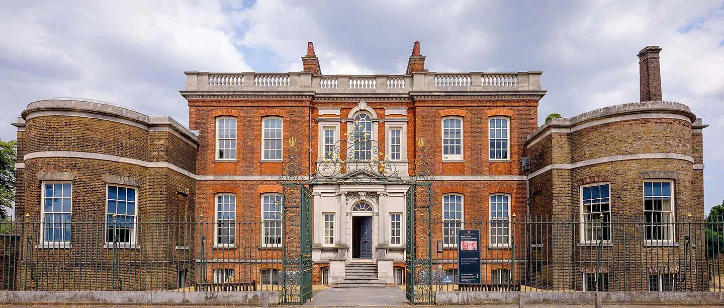 The red-brick front of Ranger's House with its bow-fronted wings, stone doorcase and balustraded roof, behind green and gilt railings and gates