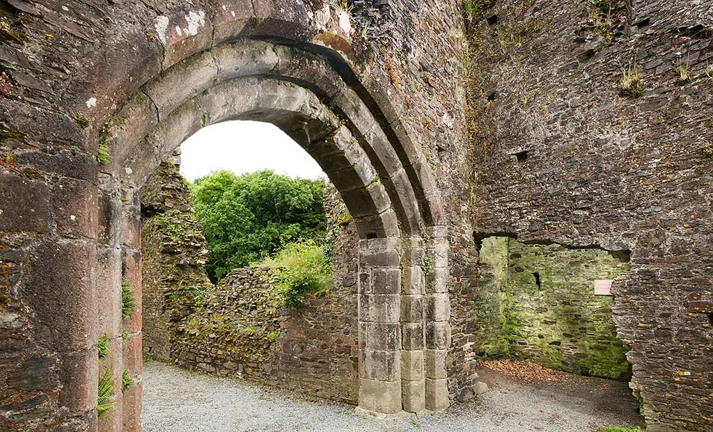A pointed stone arch inside Restormel Castle framing ruined walls and trees