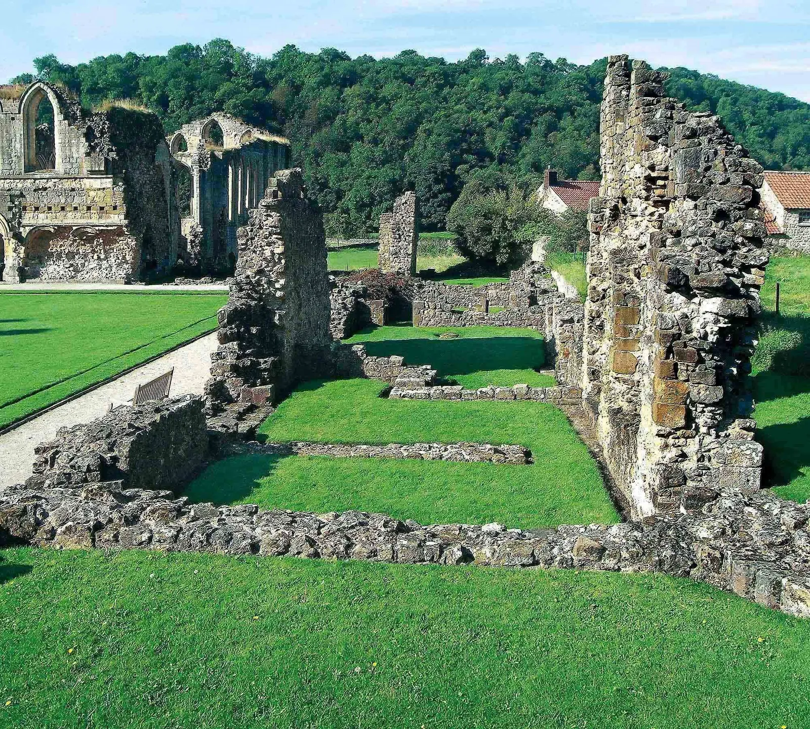 The low walls of the west range with the church ruins and wooded hillside behind