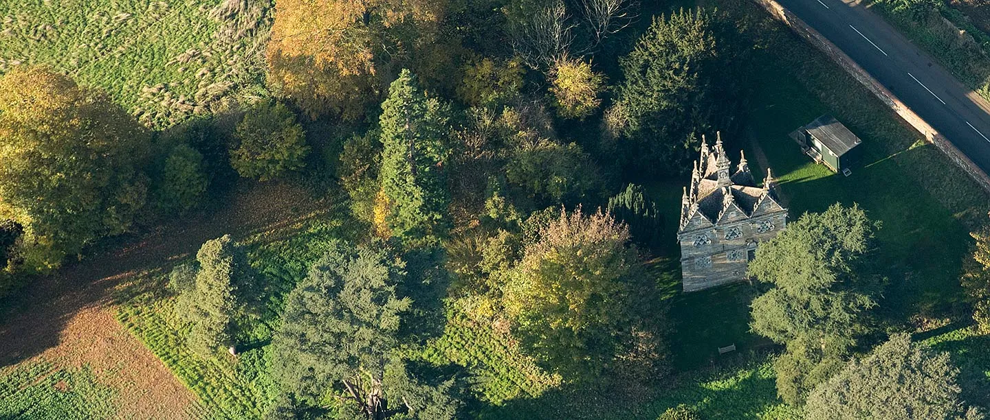 Aerial view of Rushton Triangular Lodge among autumn trees beside a country road