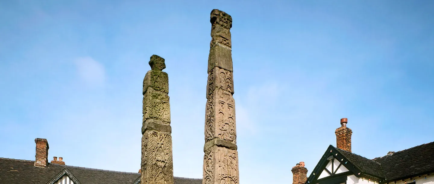 The two carved Anglo-Saxon cross shafts of the Sandbach Crosses against a blue sky above the market square