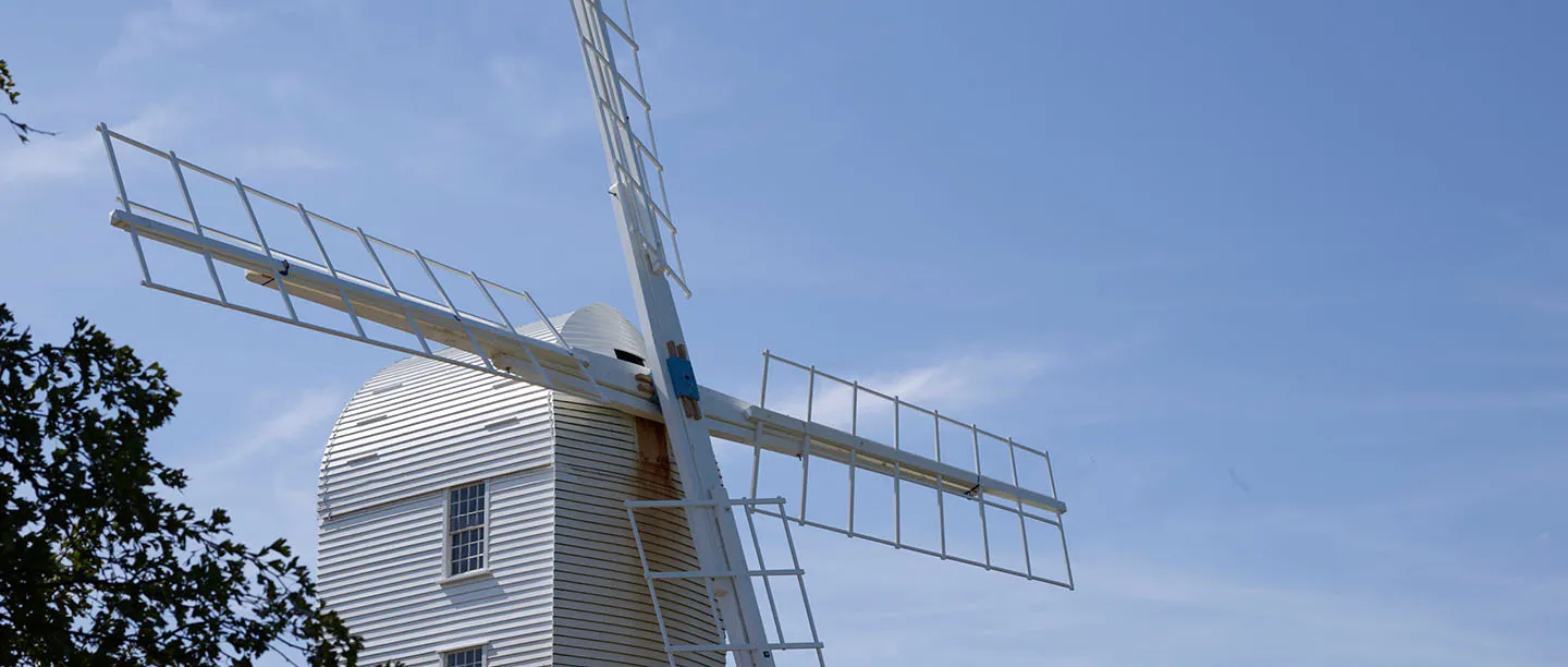 The white weatherboarded body and sails of Saxtead Green Post Mill against a clear blue sky