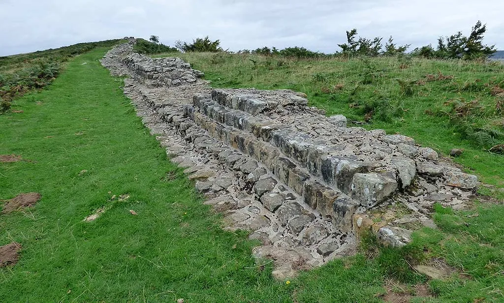 The stepped stone courses of Hadrian's Wall at Sewingshields running uphill beside a grassy path and bracken