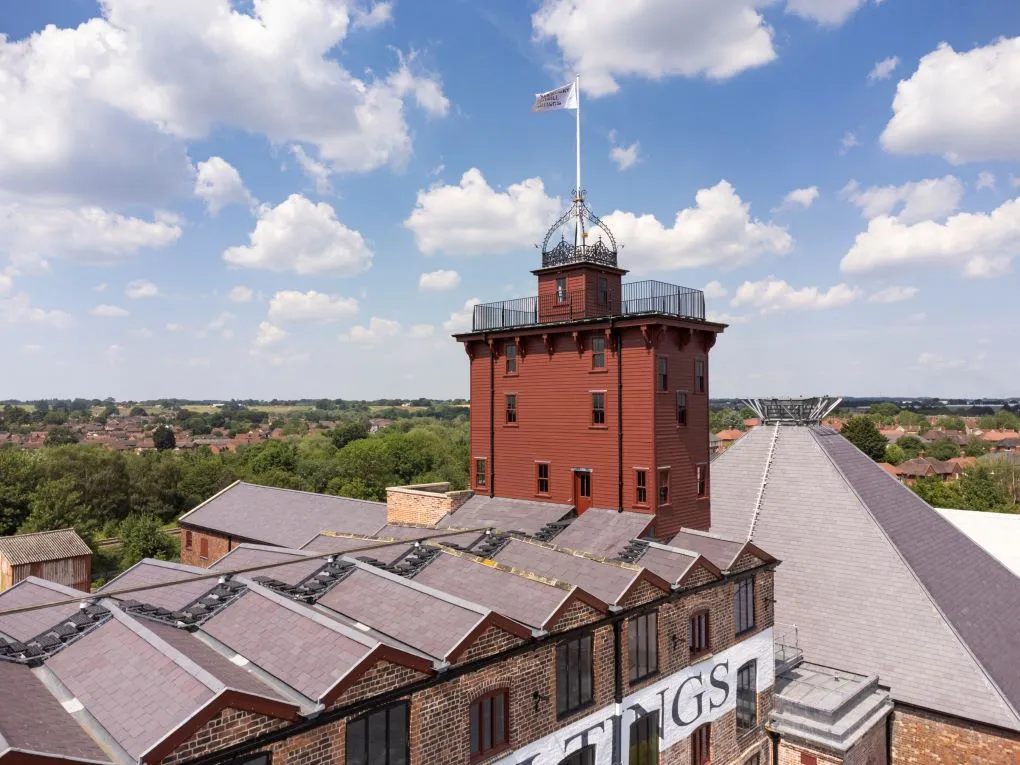 The red timber-clad tower of Shrewsbury Flaxmill Maltings with its ironwork crown and flag, above slate roofs and the town beyond