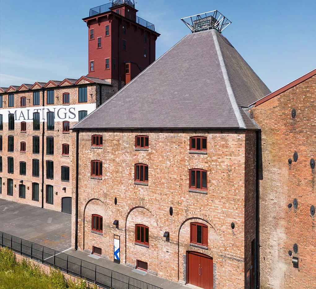 The pyramid-roofed malt kiln at Shrewsbury Flaxmill Maltings, with the red tower and the Maltings building beyond under a blue sky