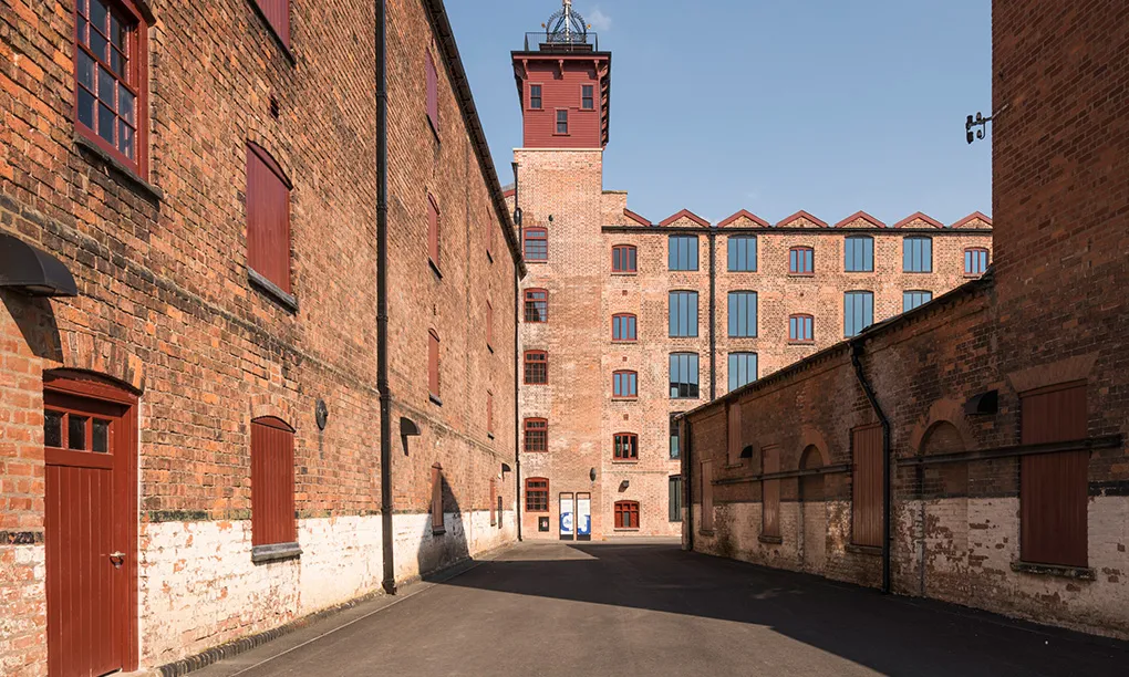 A yard between red-brick warehouses at Shrewsbury Flaxmill Maltings, leading to the five-storey main mill with its red timber-clad tower