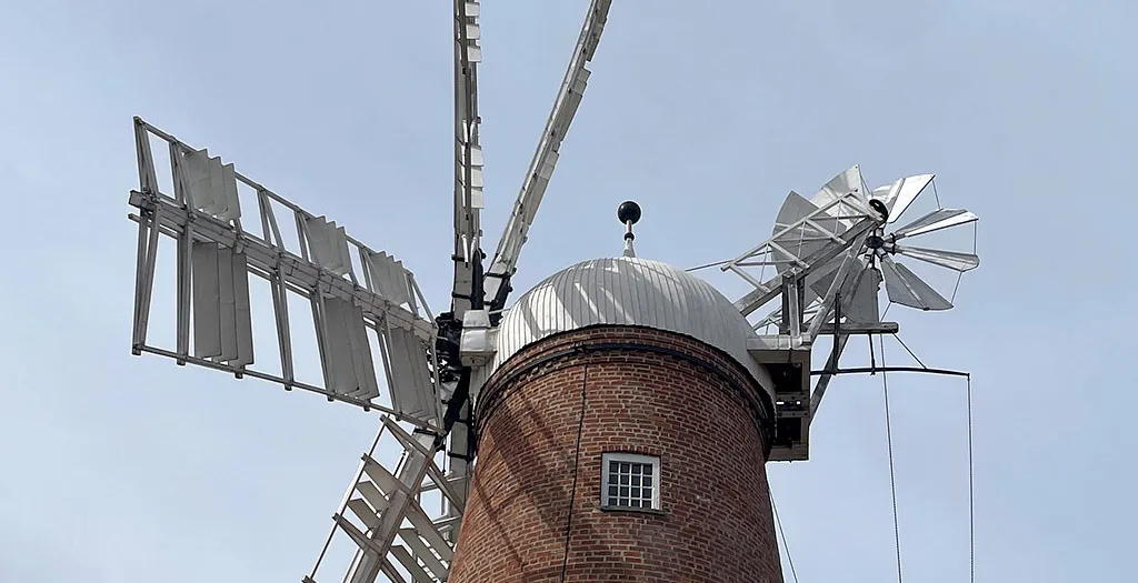The domed white cap of Sibsey Trader Windmill with its sails and fantail against a pale sky