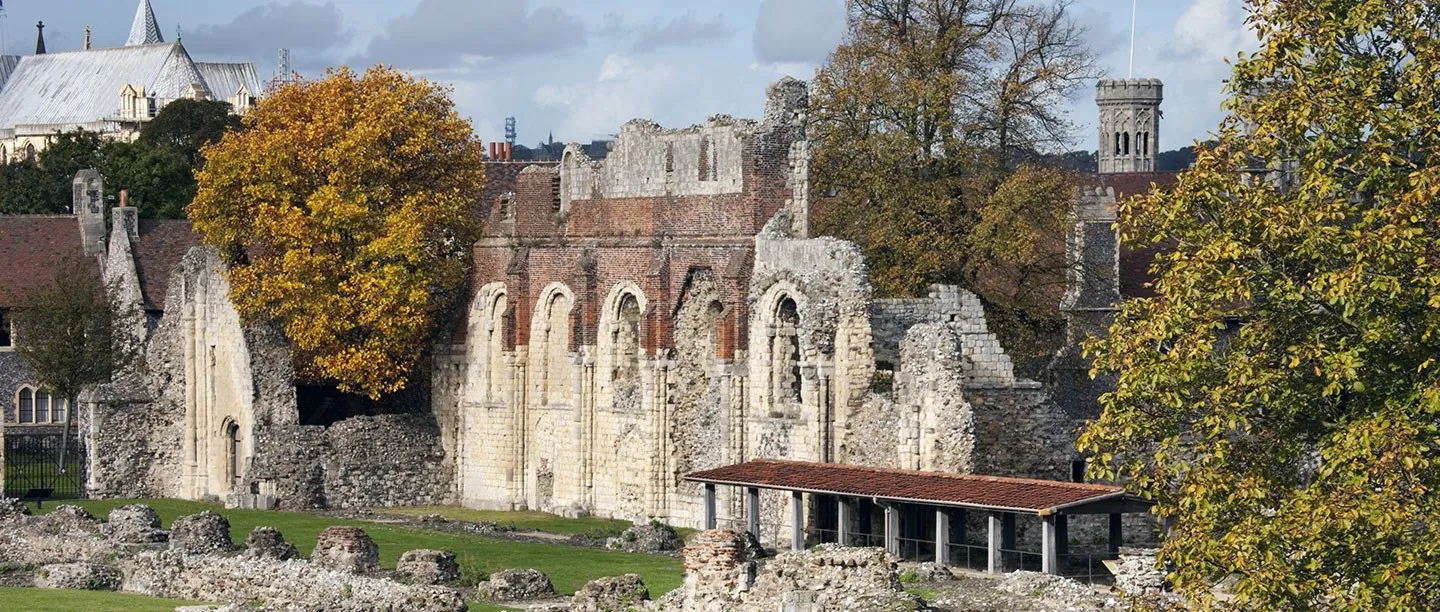 The ruined nave wall of St Augustine's Abbey with an autumn tree and Canterbury Cathedral behind