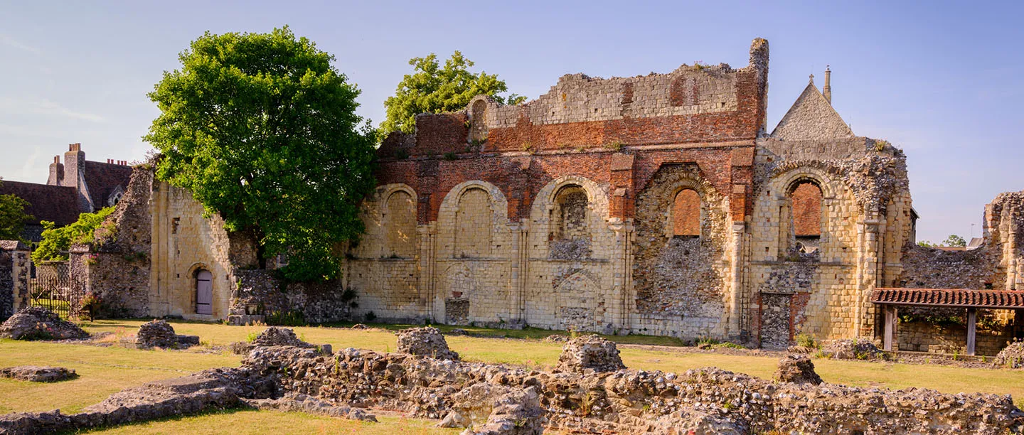 Flint and brick ruins of St Augustine's Abbey and a lawn of low foundations in evening sun