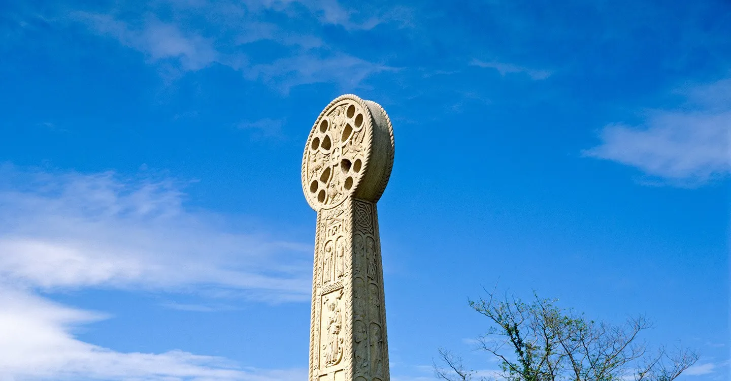 St Augustine's Cross, a tall carved stone cross with a wheel head and figures of saints, against a deep blue sky