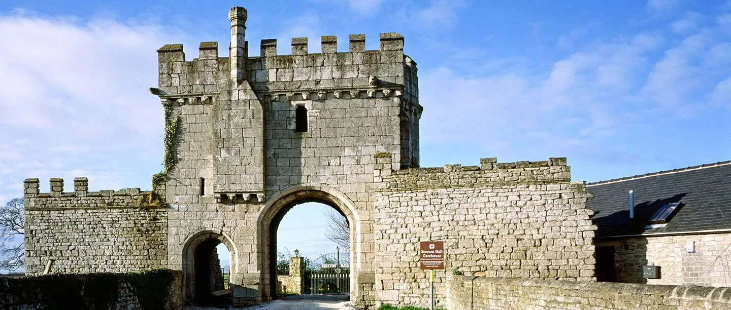 Steeton Hall Gateway, a battlemented limestone gatehouse with a large and a small arch, against a blue sky with white clouds