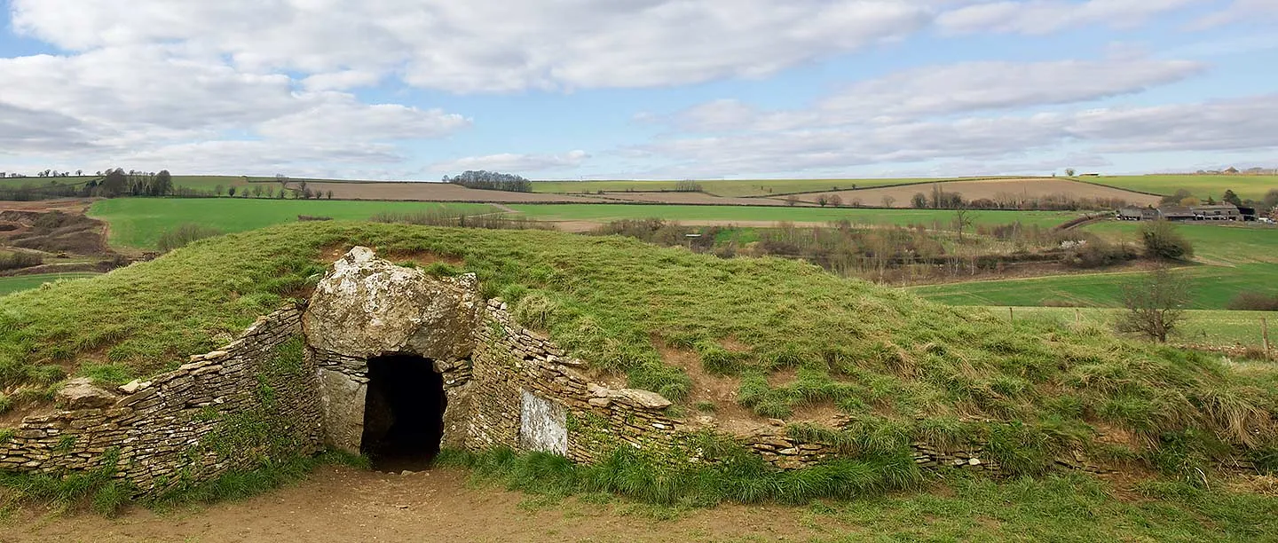 The stone-lined entrance of Stoney Littleton Long Barrow set into its grassy mound, with rolling Somerset fields beyond