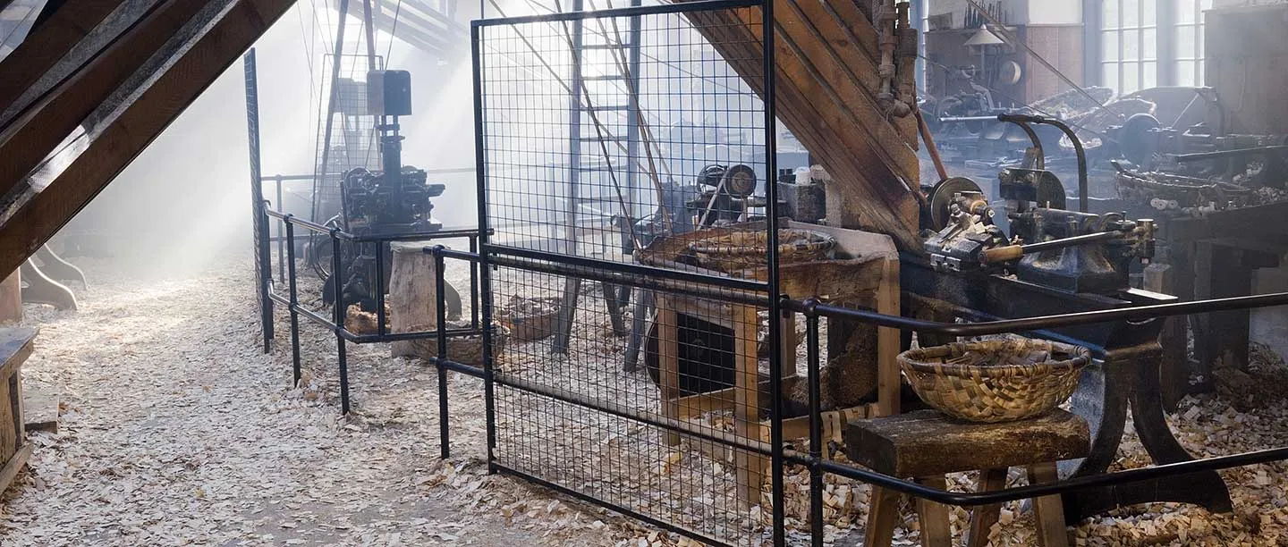 Sunlight streaming through dusty air across lathes, railings and wood shavings in the Stott Park Bobbin Mill workshop