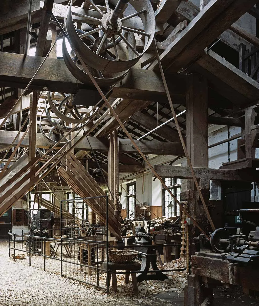 The lathe shop at Stott Park Bobbin Mill, with large iron pulley wheels, leather drive belts and timber beams above lathes and wood shavings