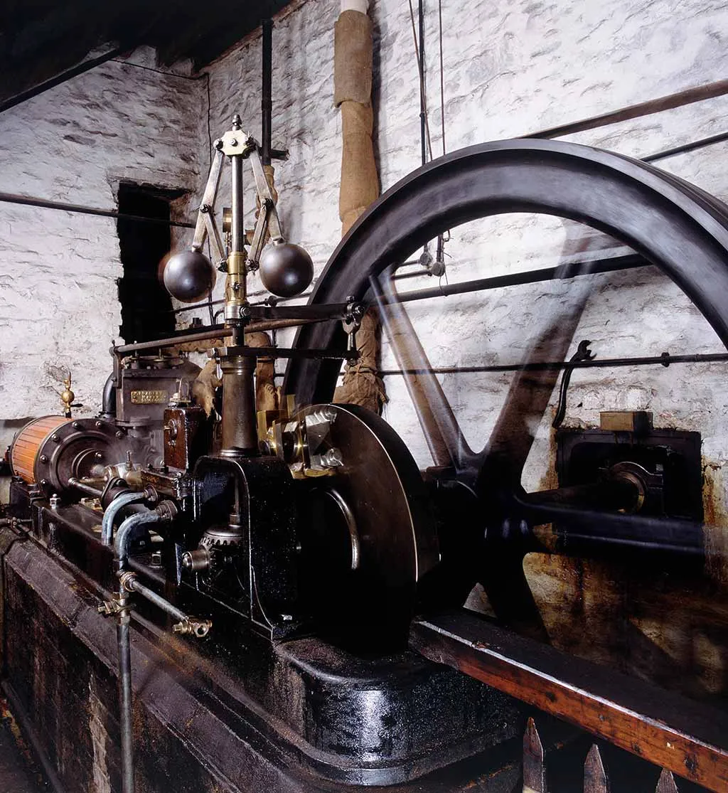 The polished steam engine at Stott Park Bobbin Mill, with its large black flywheel and brass governor against whitewashed stone walls