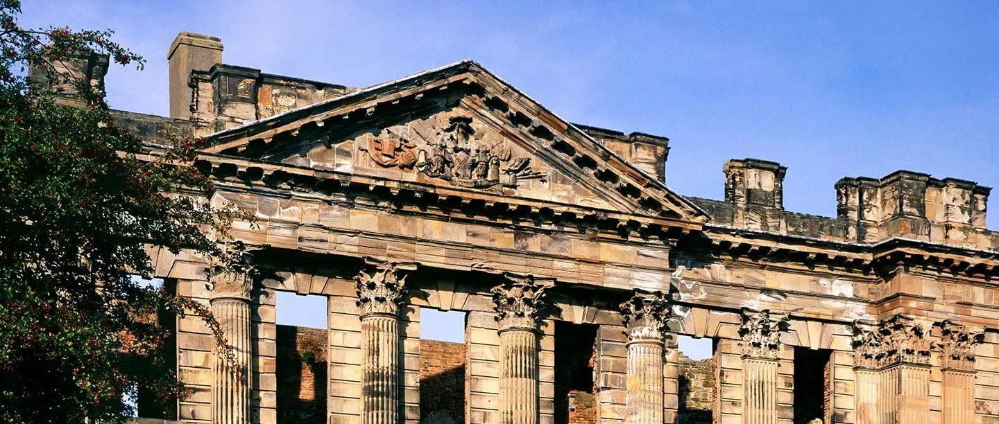 The carved pediment and Corinthian columns of Sutton Scarsdale Hall's ruined front beside a hawthorn tree in berry