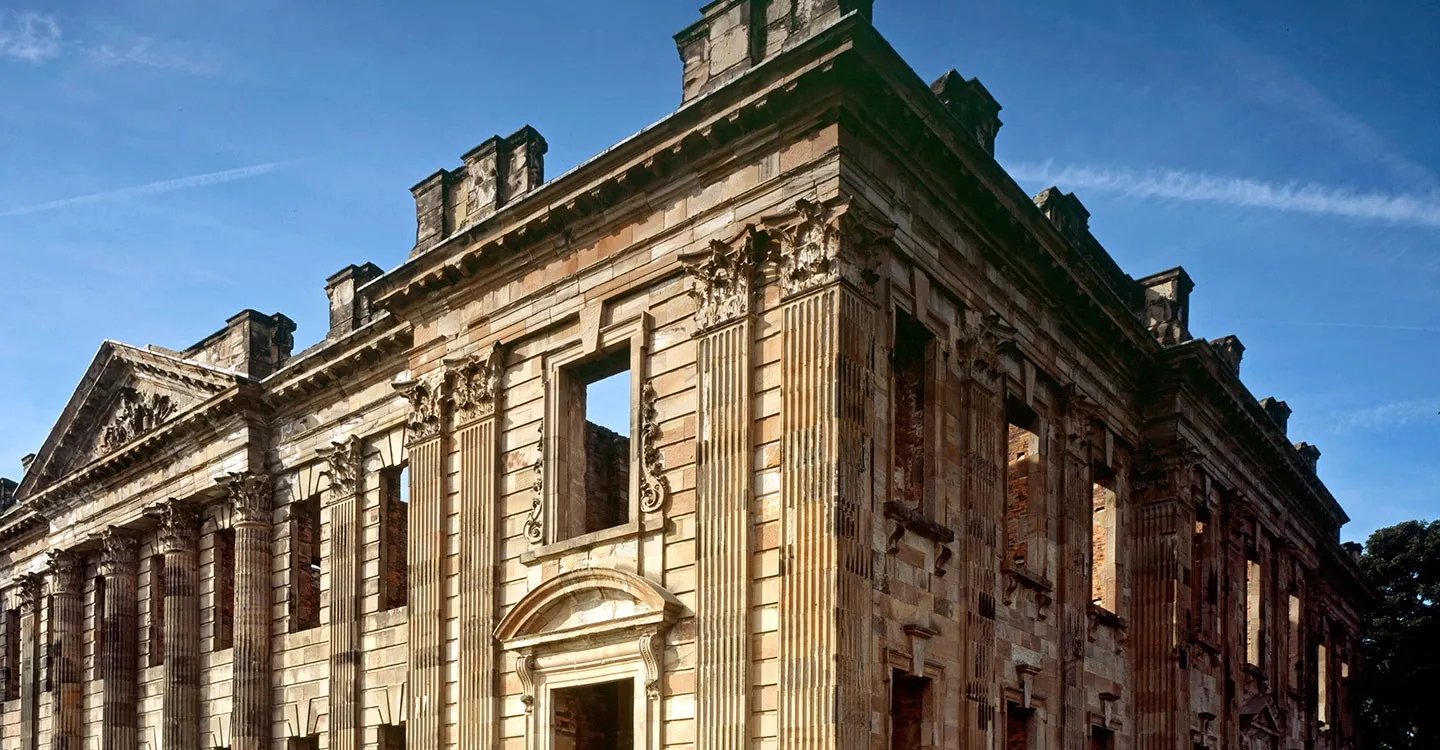The roofless Georgian front of Sutton Scarsdale Hall with fluted Corinthian columns and a carved pediment against a blue sky