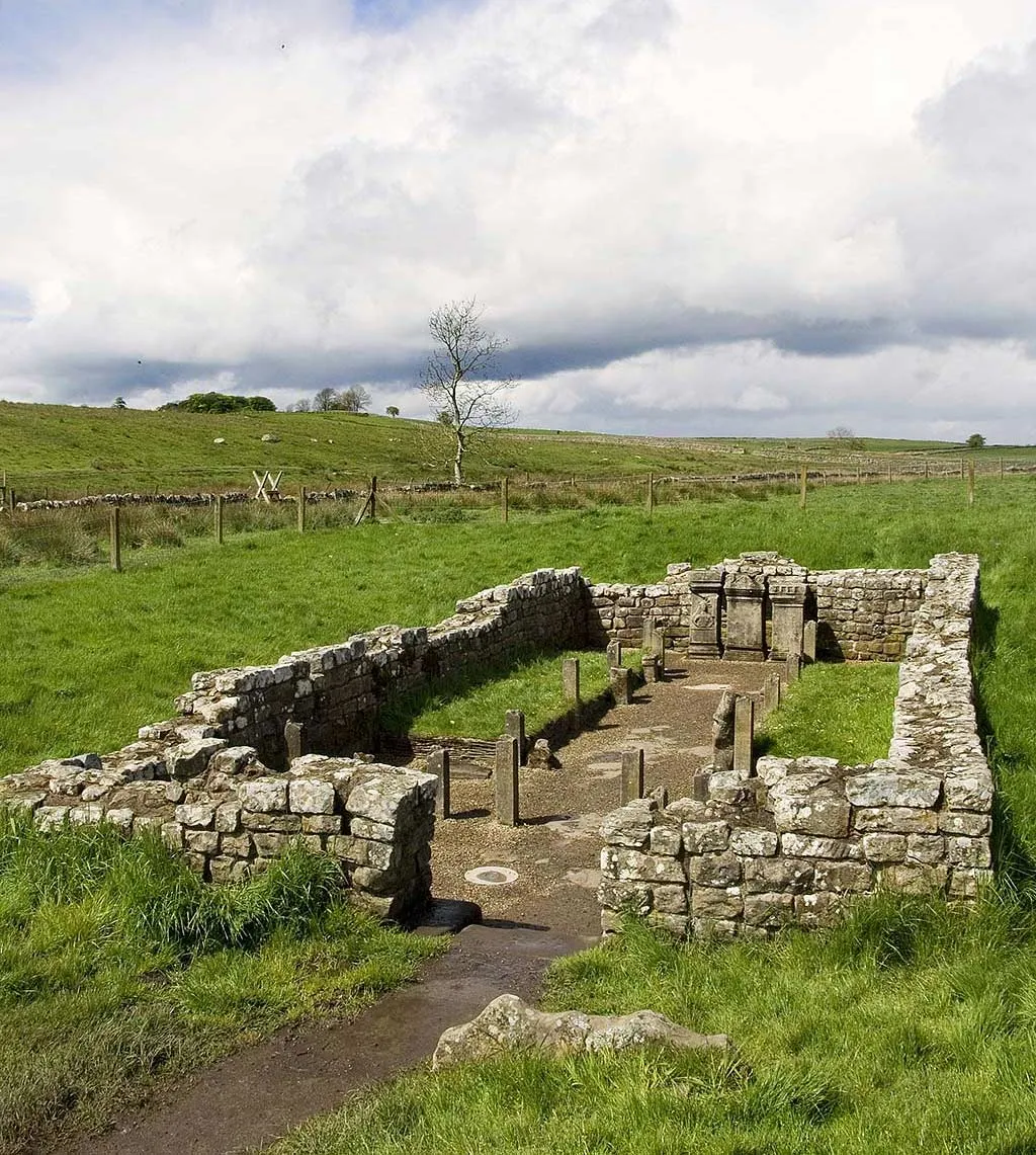 The Temple of Mithras at Carrawburgh seen from its entrance, with stone benches along the nave and three altars in the shrine, on open moorland