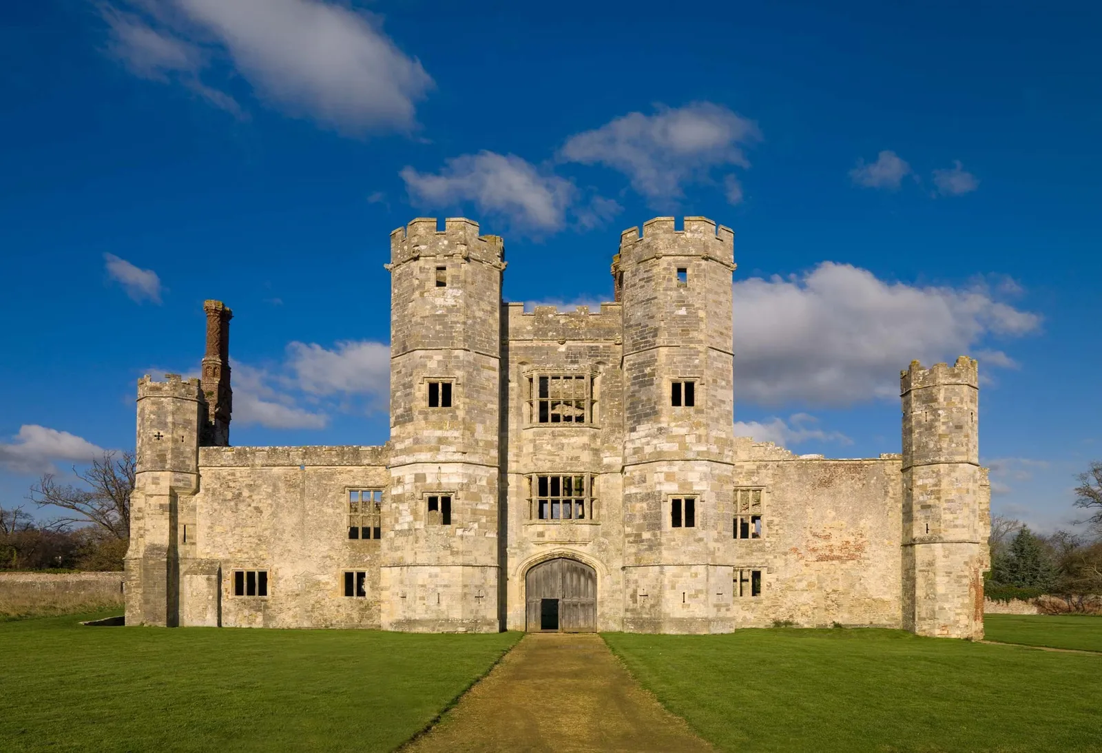 The battlemented Tudor gatehouse of Titchfield Abbey with its octagonal turrets and a gravel path across the lawn, under a blue sky