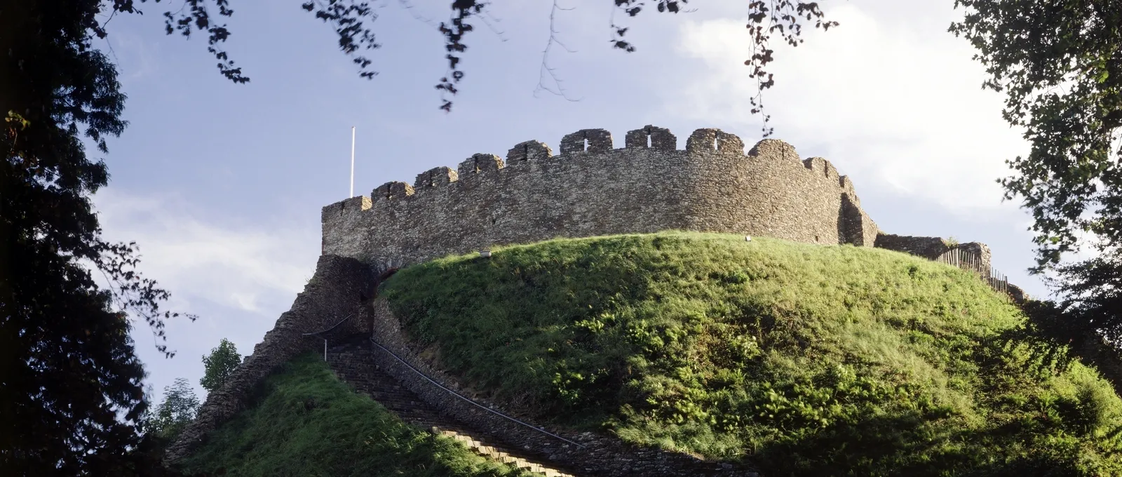 The battlemented keep on its grassy motte framed by overhanging branches