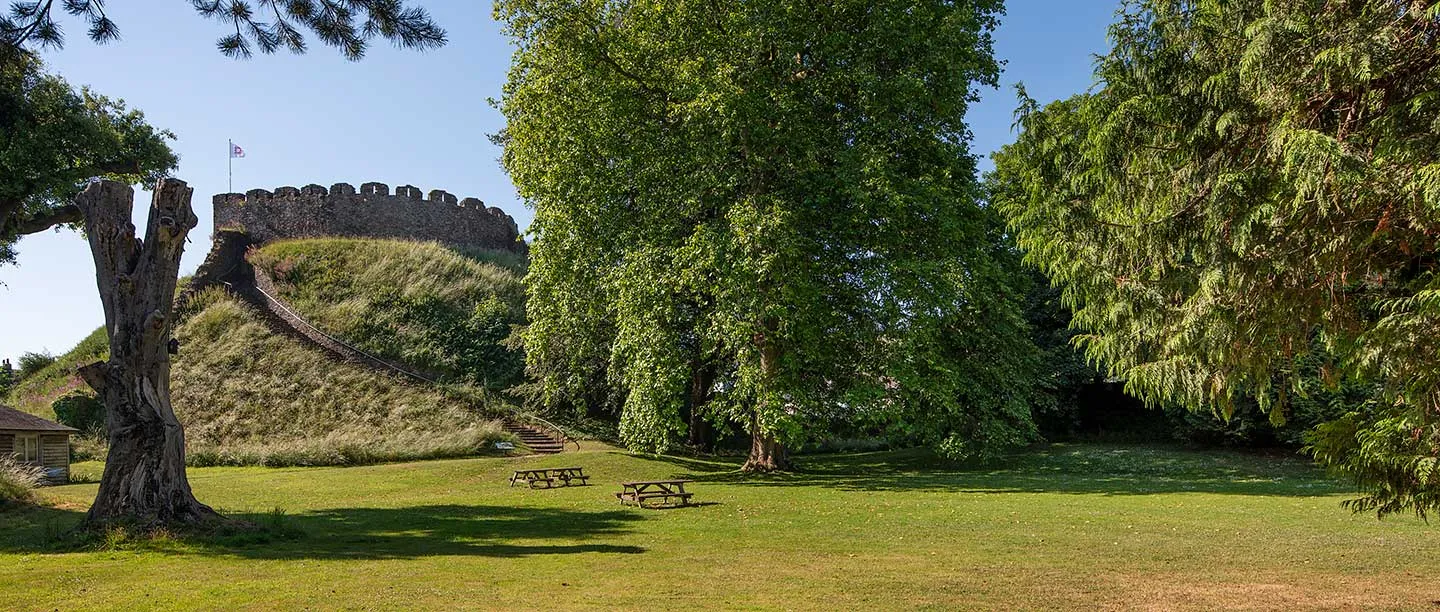 The motte and battlemented keep seen across the bailey lawn, with picnic tables and an old tree stump