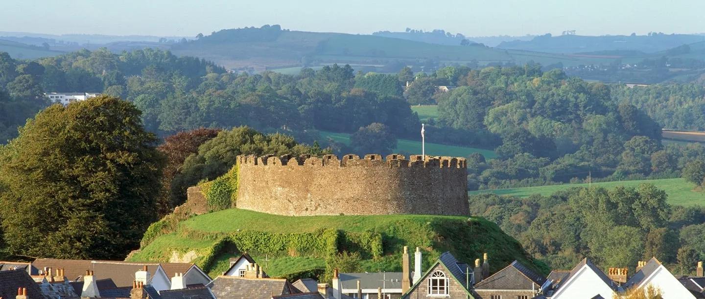 The round shell keep of Totnes Castle on its green motte above the town rooftops, with wooded hills beyond