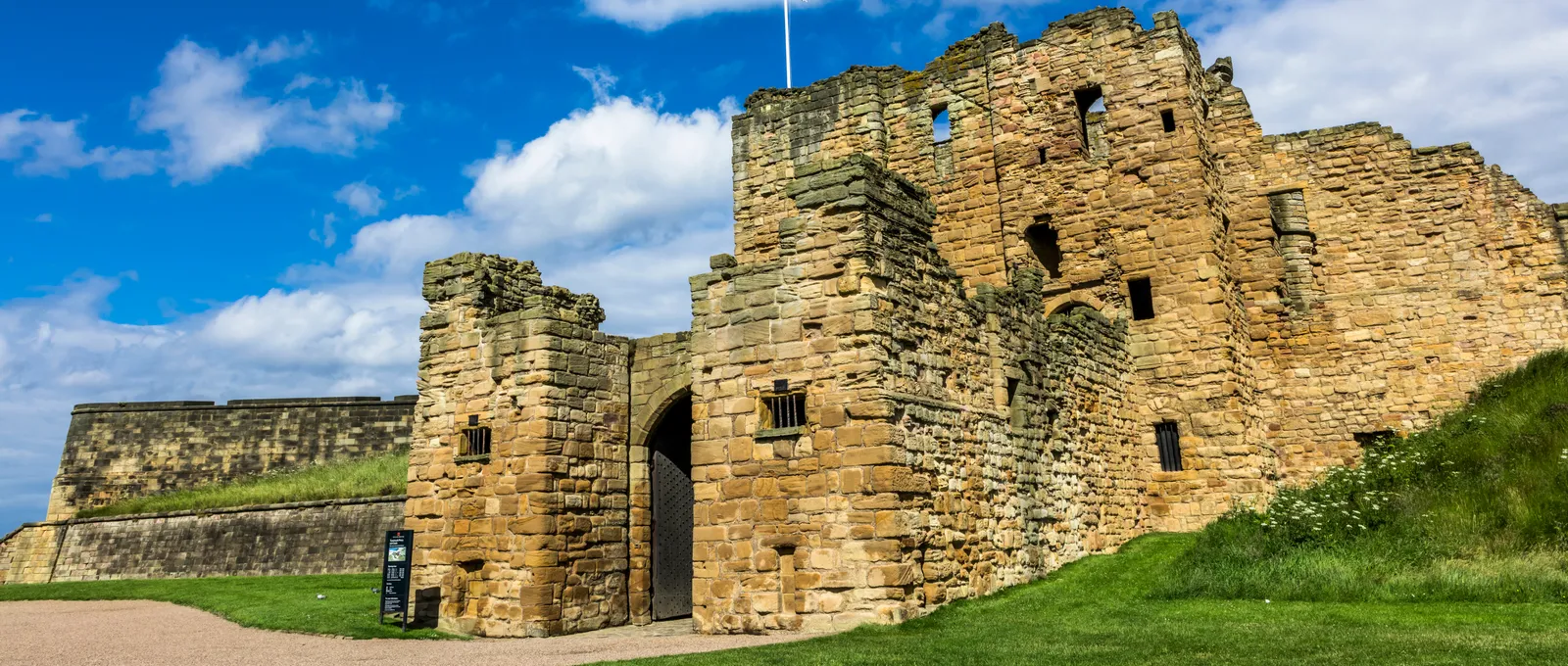The castle gatehouse and barbican in warm sandstone under a bright blue sky